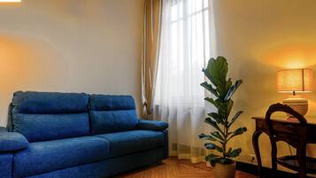 A room with a blue sofa, a wooden floor, a potted plant, a lamp, and a chair.