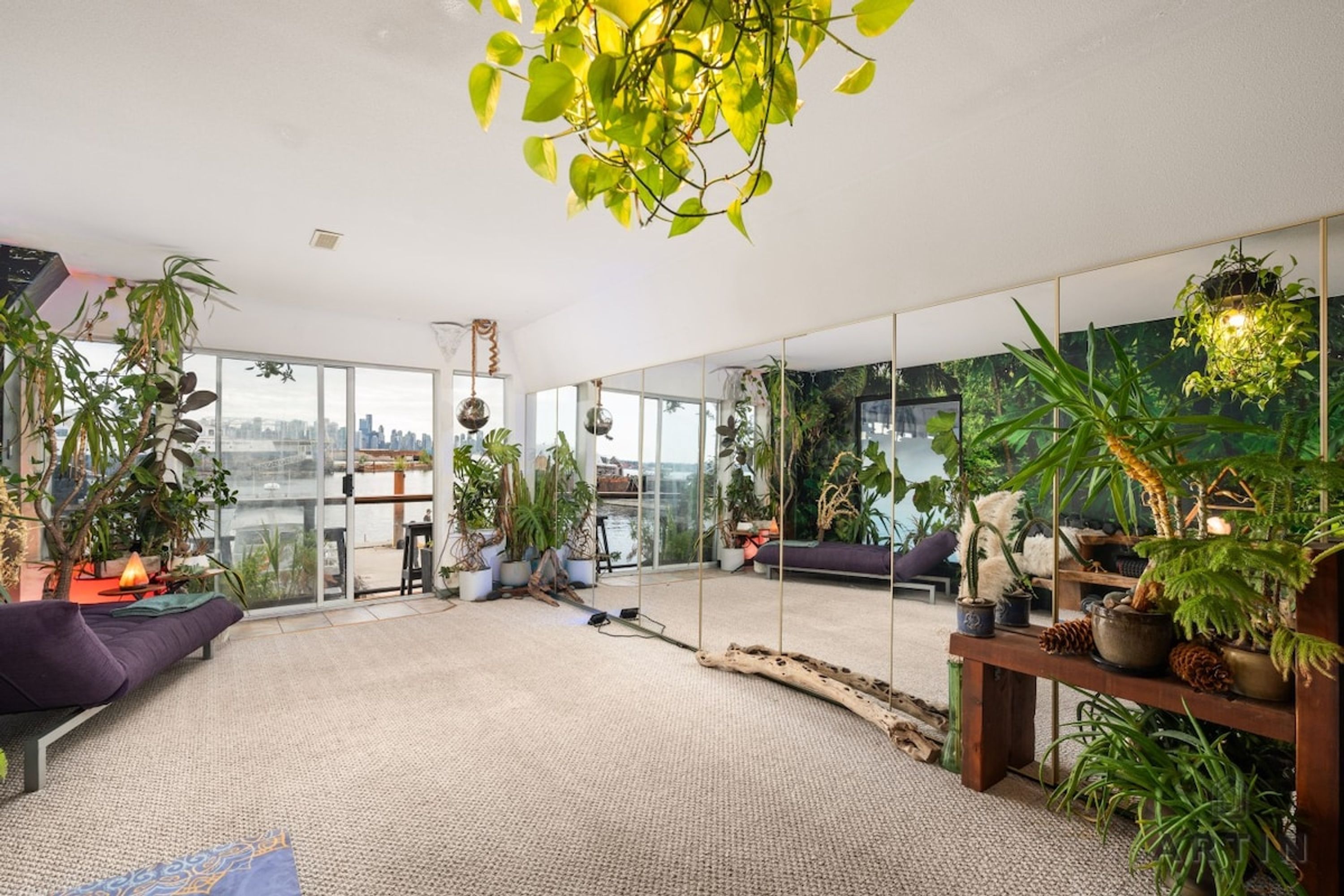 A modern living room with a large window, a sofa, and various plants.