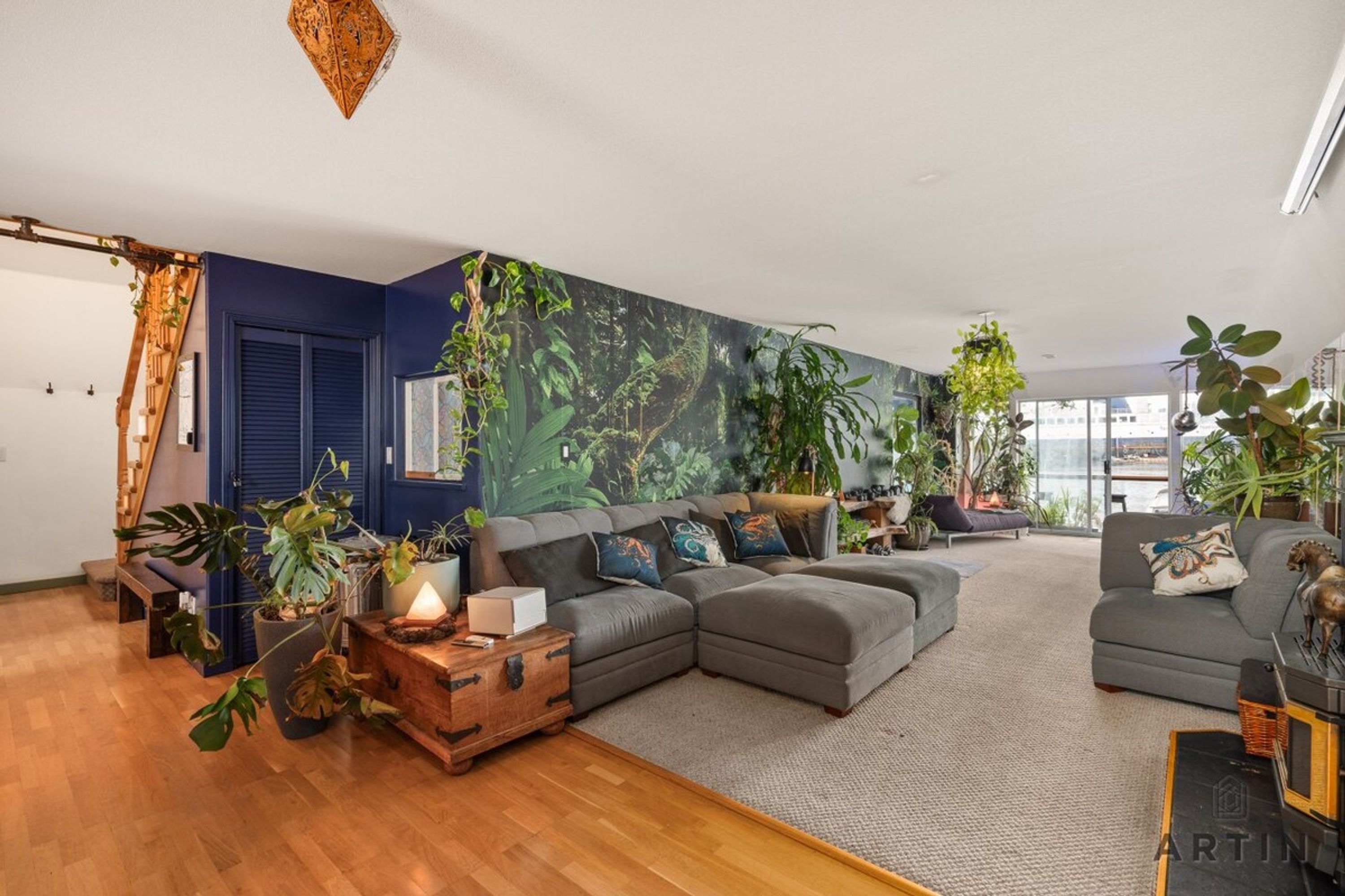 A modern living room with a sectional sofa, a wooden coffee table, and various plants.