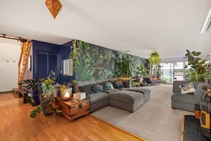 A modern living room with a sectional sofa, a wooden coffee table, and various plants. - The Octopus Garden One-of-a-kind 2BR Float Home (North Vancouver)