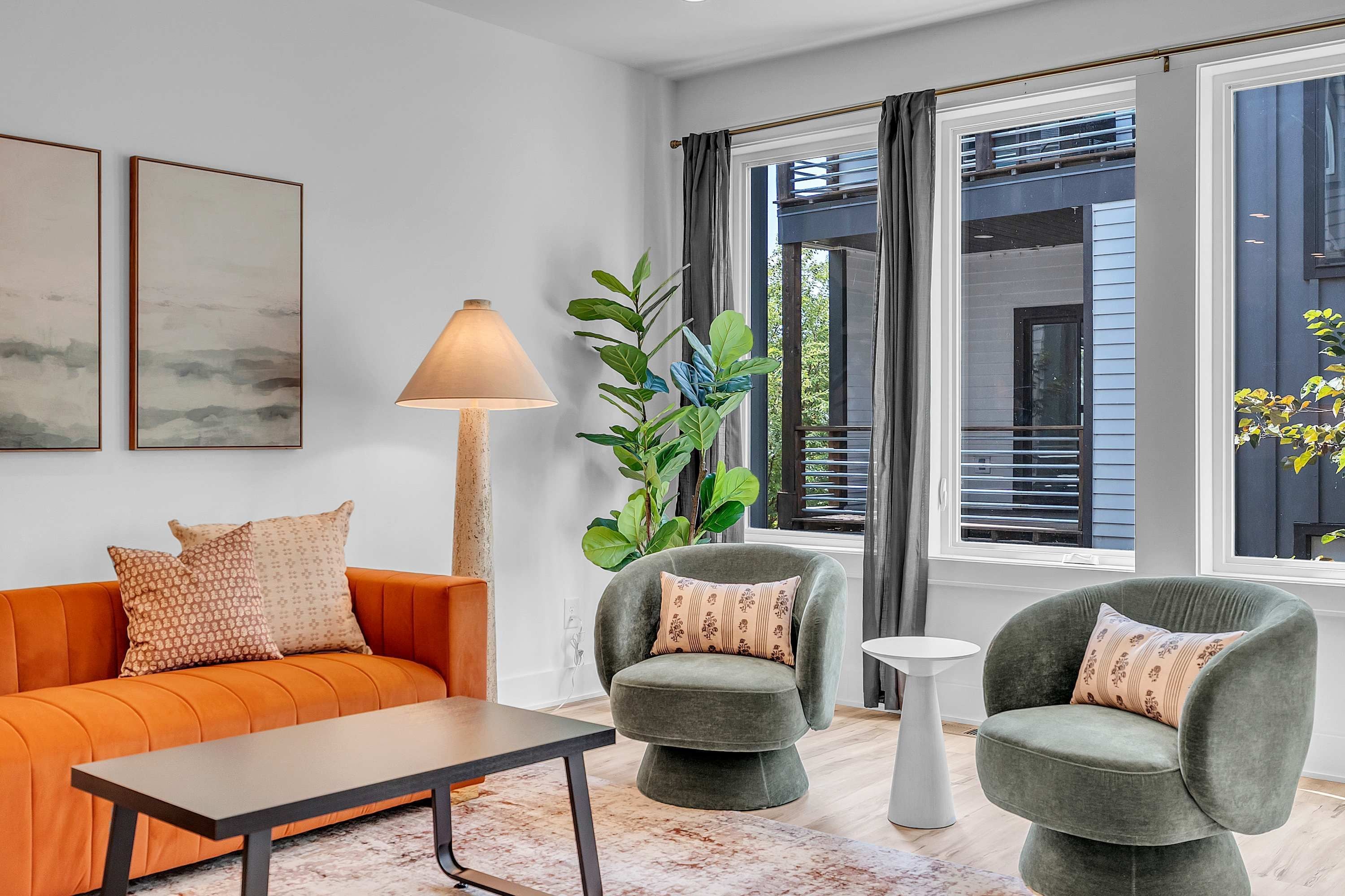 A modern living room with a sofa, two armchairs, a coffee table, a floor lamp, and a large window with curtains.