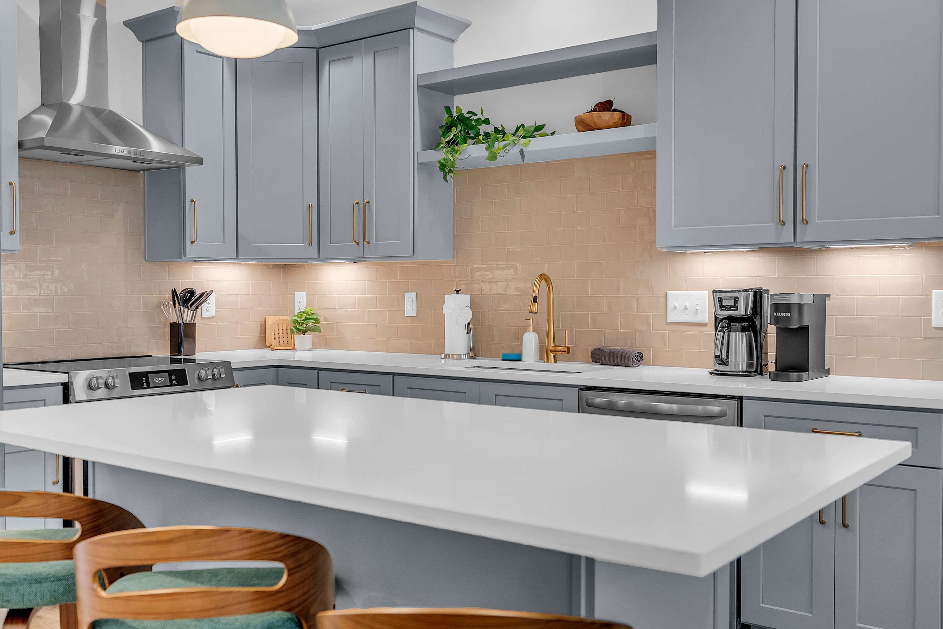 A modern kitchen with grey cabinets, a large island, and stainless steel appliances.