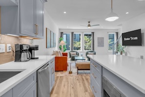 Una cocina moderna con armarios grises, una cafetera y un área de comedor con un sofá y un televisor que muestra el texto 'Home Team'.