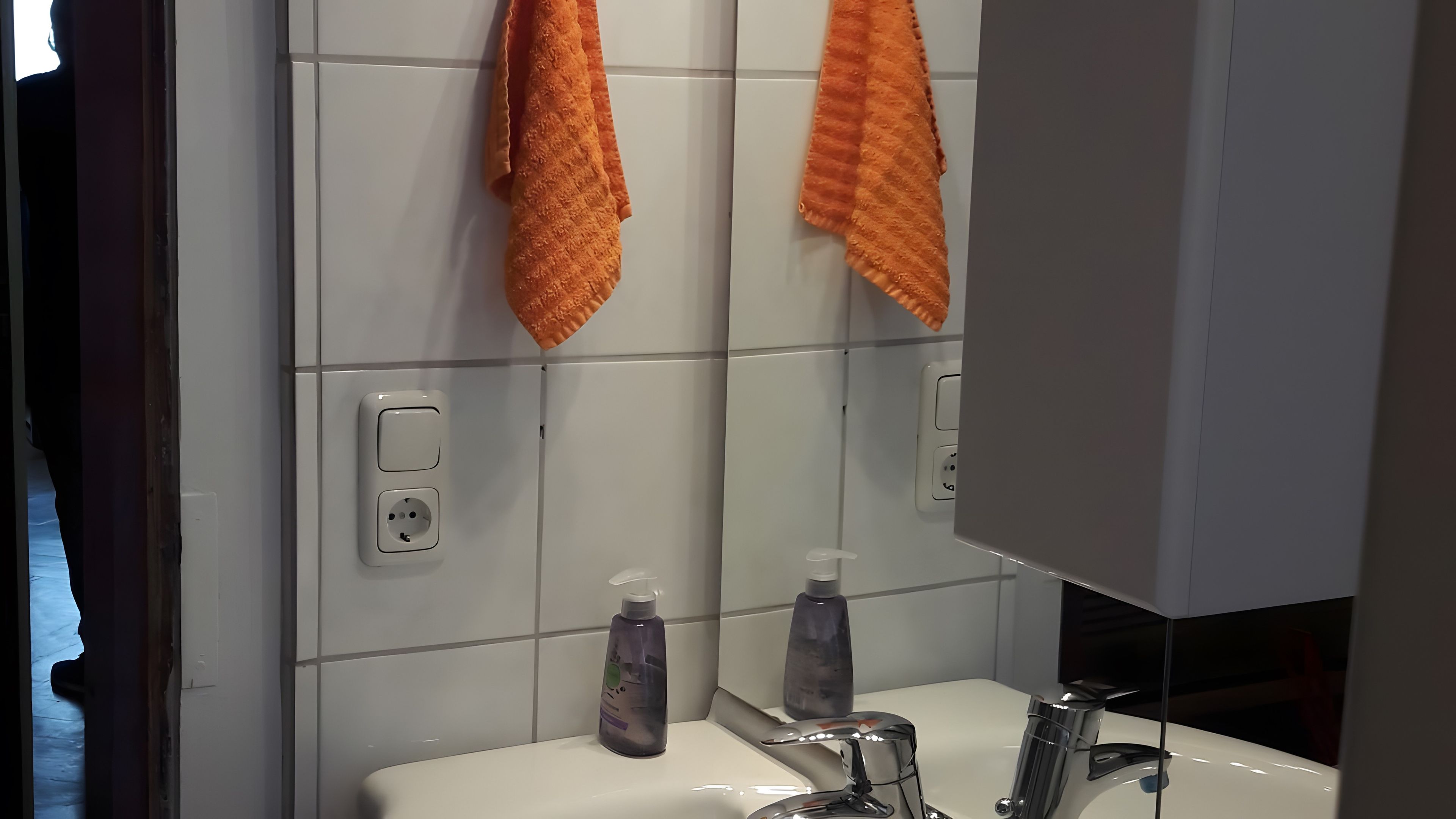 A bathroom with a white sink, two hand soap dispensers, and a mirror reflecting an orange towel.