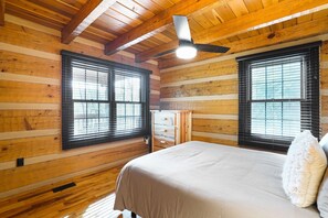Ein Schlafzimmer in einer Blockhütte mit einem Bett, einer Kommode und zwei Fenstern mit Jalousien.