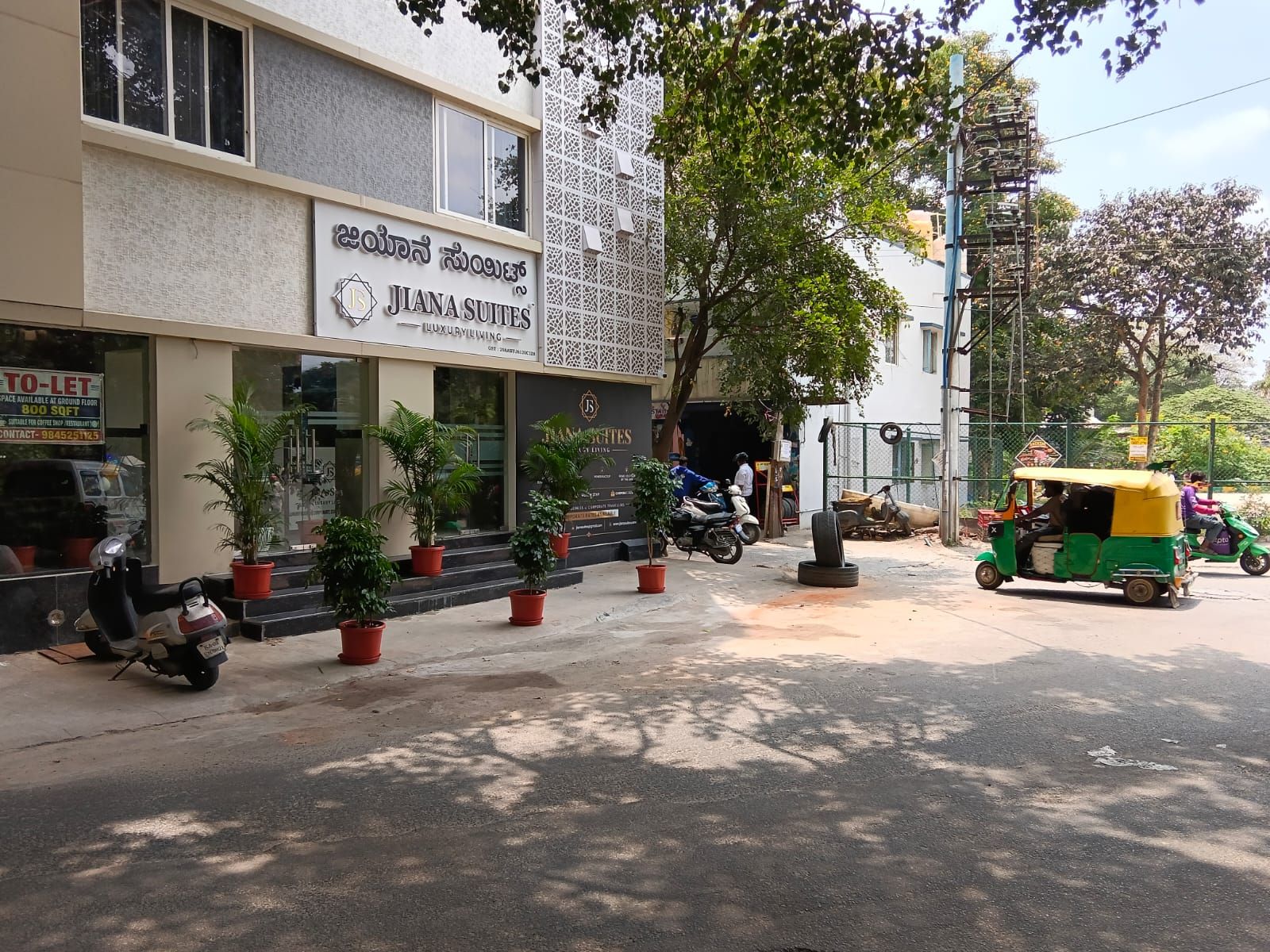 A building with a sign for 'JIANA SUITES' and a 'TO-LET' sign. There are potted plants in front of the building.