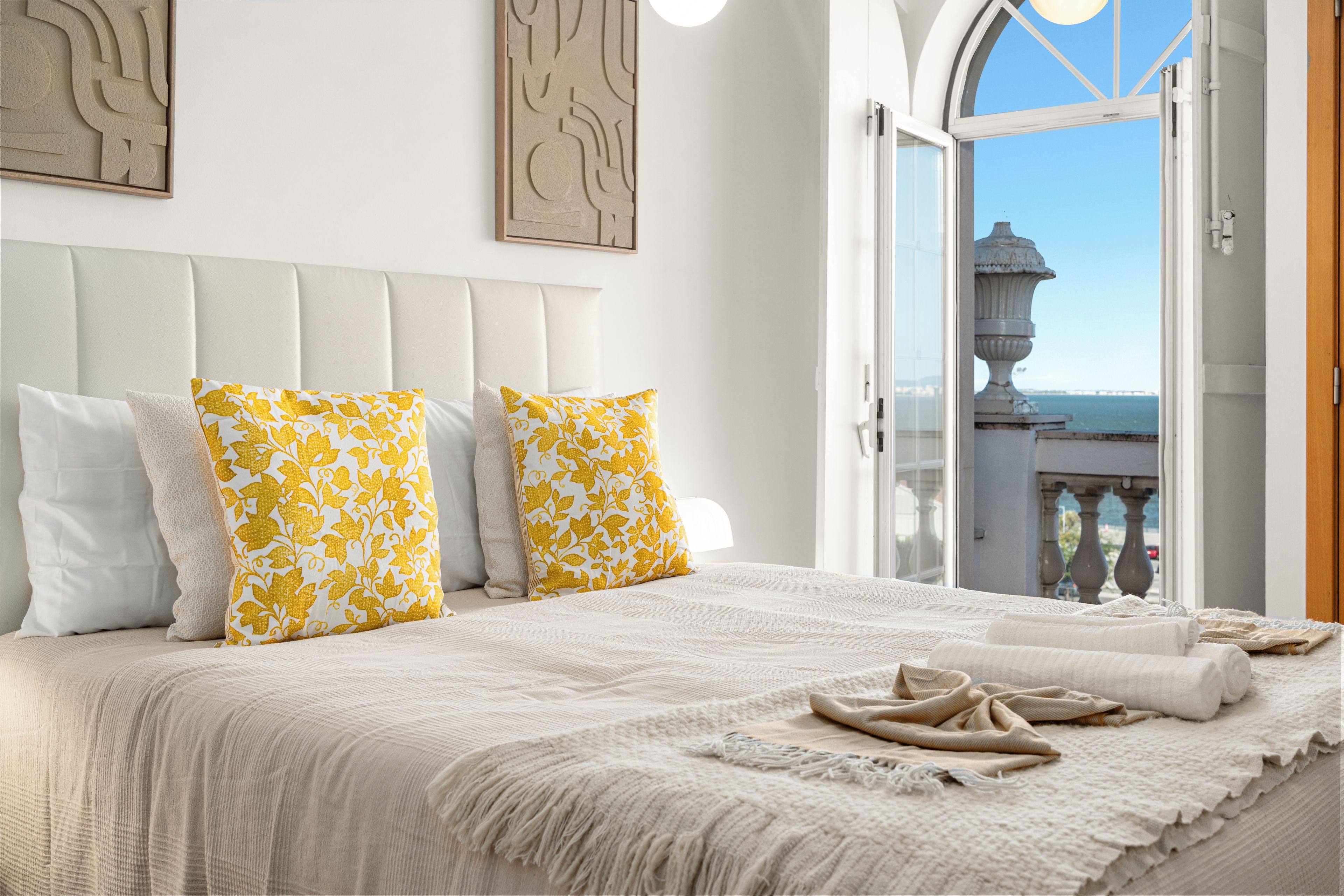 A hotel room with a large bed, white bedding, and a view of the sea through an open door.