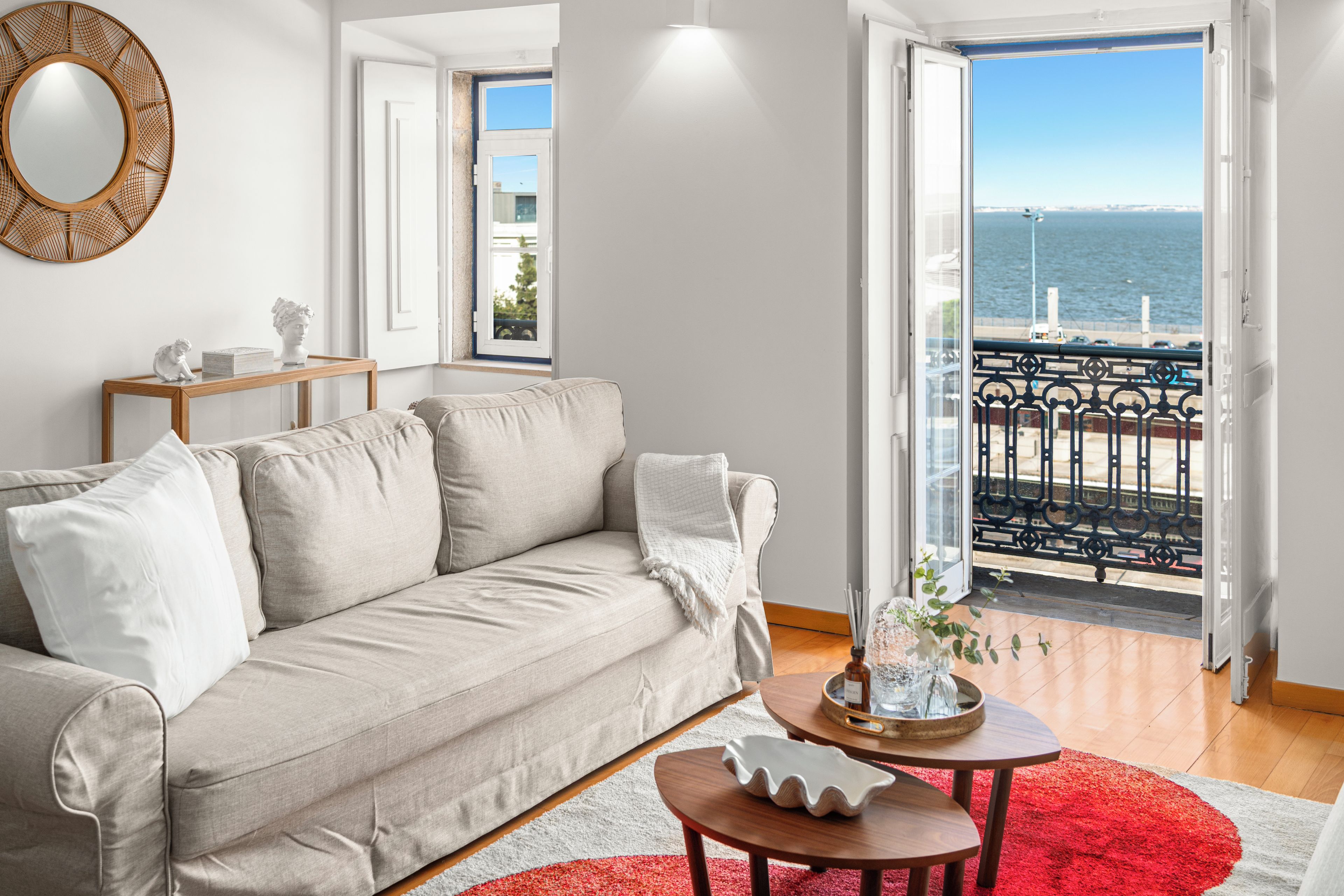 A living room with a sofa, a coffee table, and a view of the sea through a balcony.