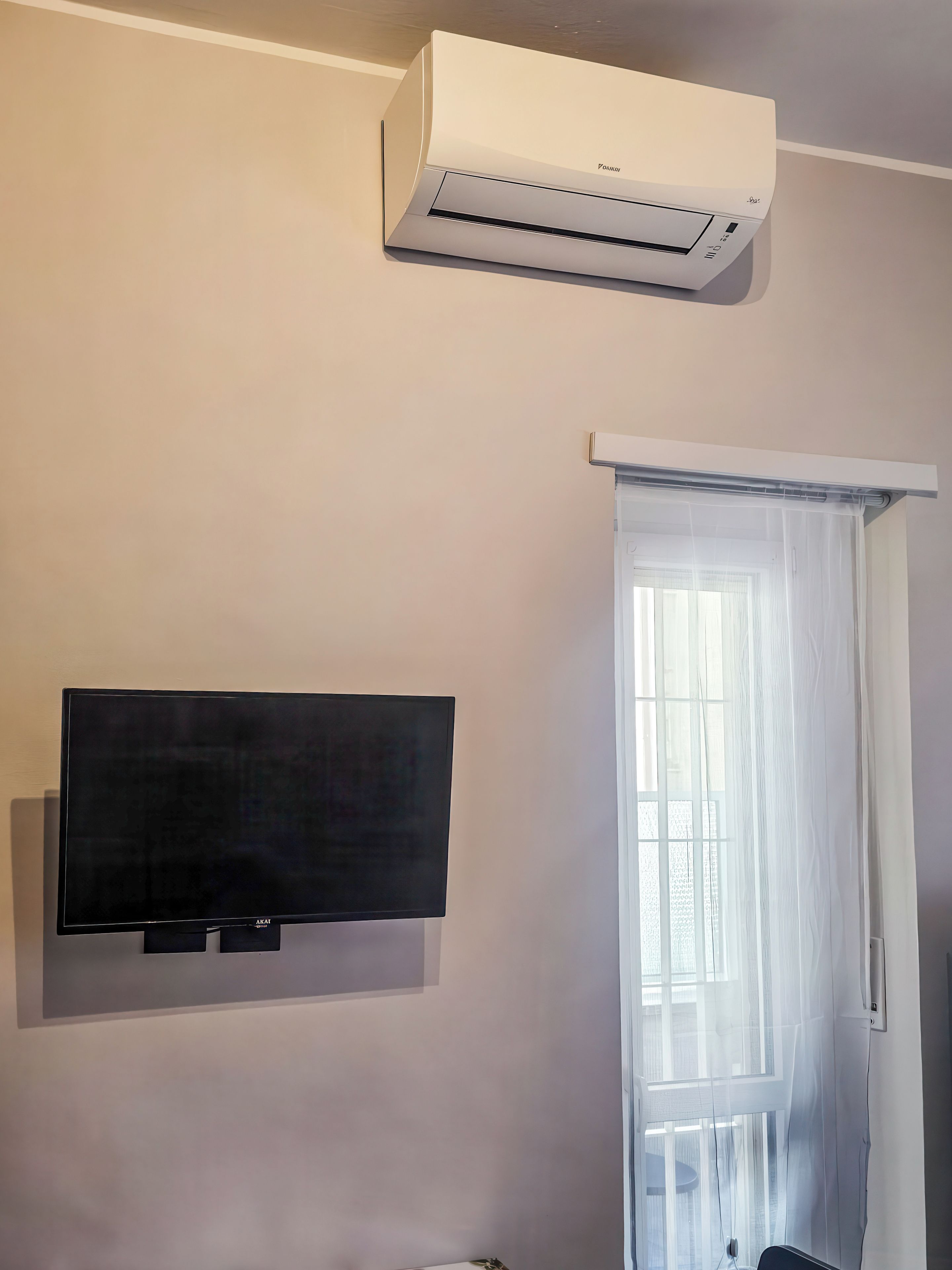 Habitación con aire acondicionado instalado, televisor de pantalla plana y ventana con cortinas translúcidas.