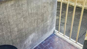 Un rincón de una habitación con suelo de baldosas, una ventana con panel de vidrio texturizado y una barandilla de metal.