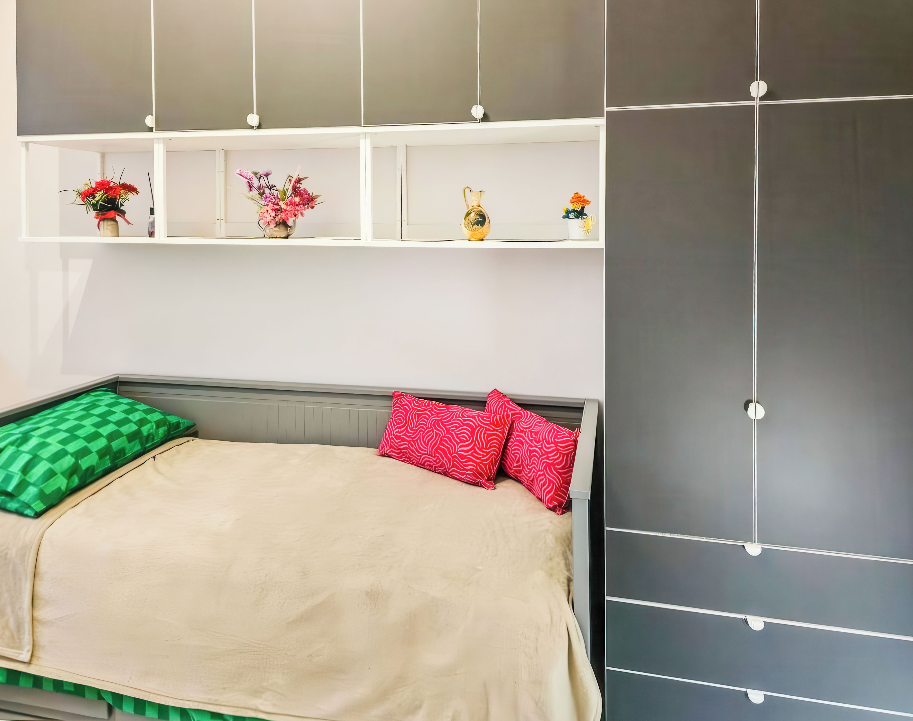 Un dormitorio con cama, almohadas, una estantería con objetos decorativos y un armario.