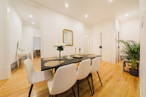 A dining area with a black table, white chairs, a vase of flowers, and a mirror on the wall. - Heart of Lisbon | Comfortable Stay for 10 w/AC (Lisbon)