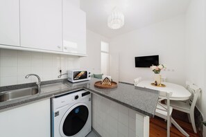 A modern kitchen with white cabinets, a built-in washing machine, a microwave, and a dining area with a table and chairs. - Elegant Central Lisbon Stay w/AC at Your Doorstep (Lisbon)