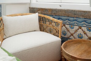 A wicker chair with a textured cushion, a wooden bowl, and a tiled wall with floral patterns. - Elegant Central Lisbon Stay w/AC at Your Doorstep (Lisbon)