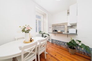 A white dining table with chairs, a vase with flowers, and a window with patterned curtains. - Elegant Central Lisbon Stay w/AC at Your Doorstep (Lisbon)