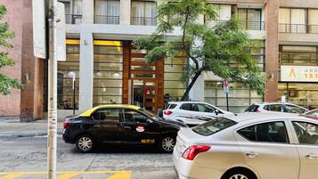 Un edificio de varios pisos con una entrada moderna, autos estacionados y un letrero visible de un hotel.