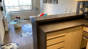 A modern kitchen with wooden cabinets, a glass-top dining table, and a built-in coffee machine. - Cozy 1-bedroom apartment in beautiful Santiago with AC (Santiago)