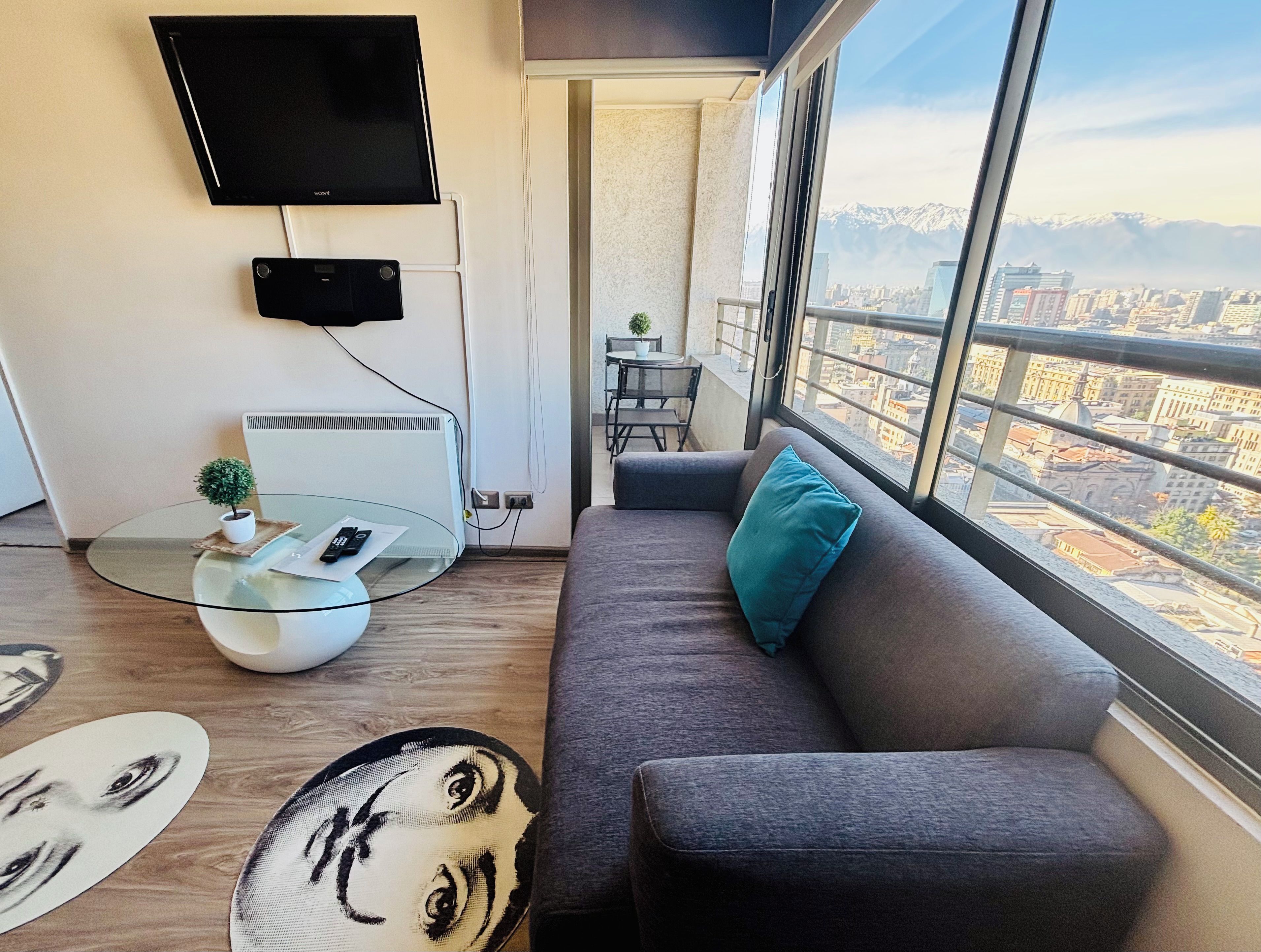 Una sala de estar moderna con un sofá, una mesa de centro de vidrio, una planta pequeña y un televisor de pantalla plana montado en la pared.
