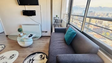 Una sala de estar moderna con un sofá, una mesa de centro de vidrio, una planta pequeña y un televisor de pantalla plana montado en la pared.