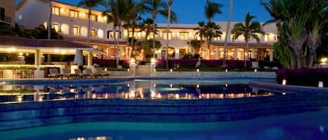 Un hôtel doté d’une piscine, de palmiers et d’une façade bien éclairée.
