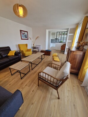 A living room with a black sofa, yellow armchairs, a wooden coffee table, a wicker chair, and a wooden cabinet. - Large, quiet house near Nantes (Vertou)