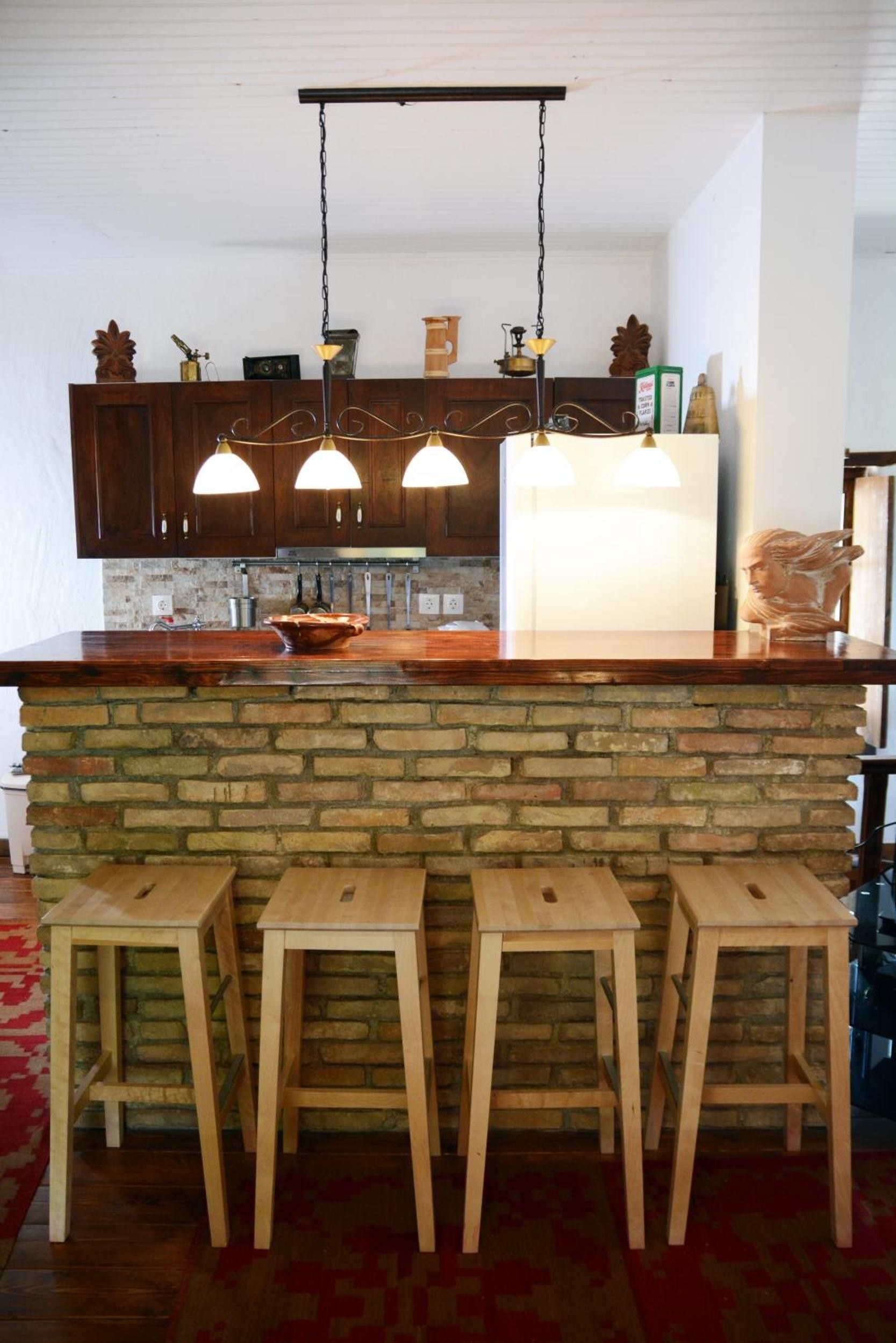 Una cocina con una isla de piedra, taburetes de madera y lámparas colgantes.