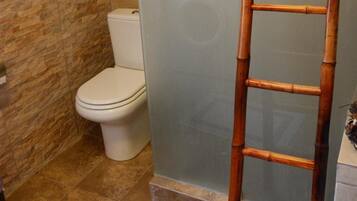 A bathroom with a toilet, a shower area with a glass door, and a bamboo ladder.