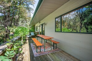 A covered outdoor patio with a wooden table and bench, surrounded by lush greenery. - Stunning 3,000 sq ft Blue Ridge Pkwy Guest House 30 Acres/Pond/Hot Tub/Game Room (Floyd)