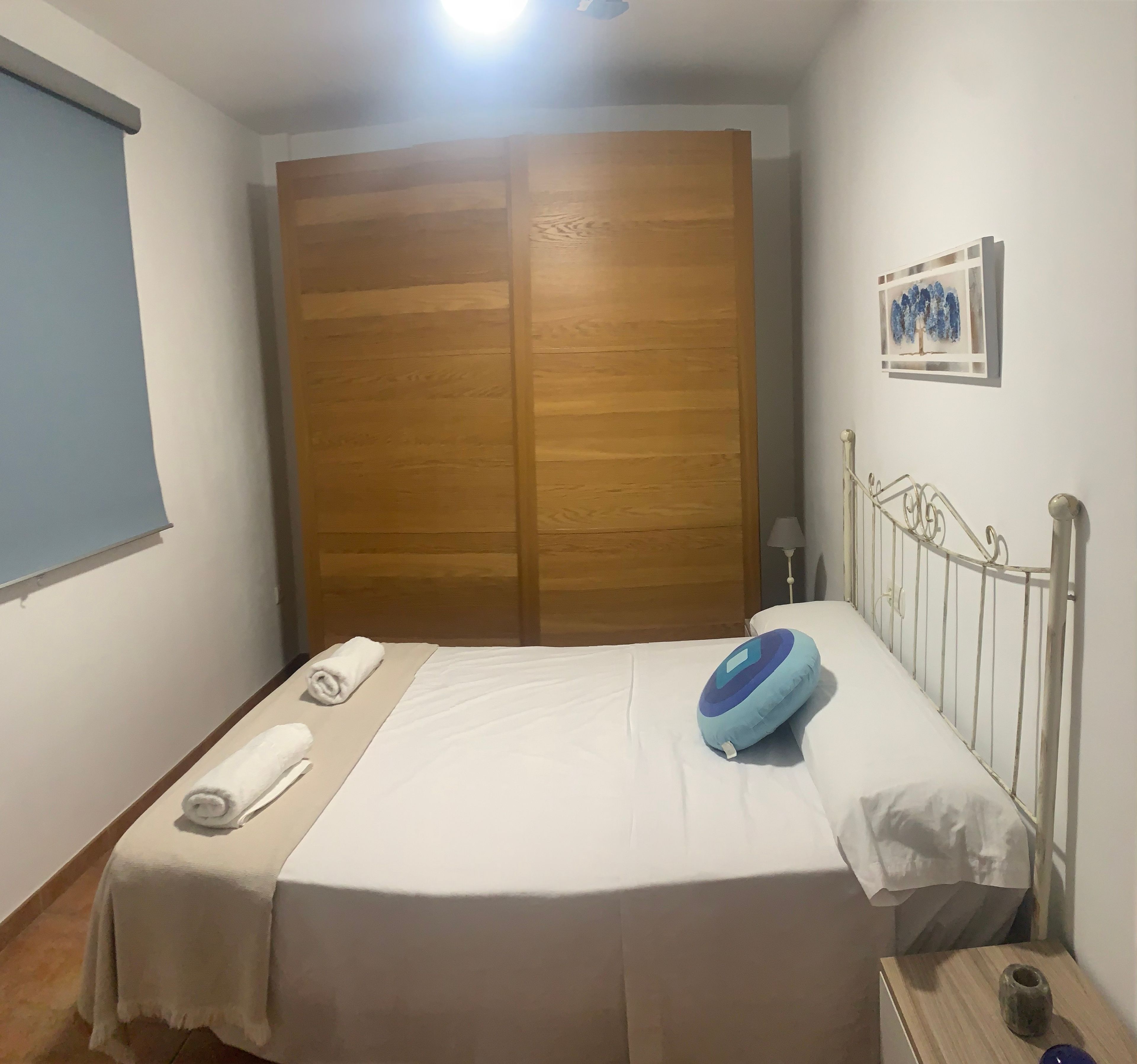 Una habitación de hotel con una cama, un armario de madera, un cuadro en la pared y una mesita de noche.