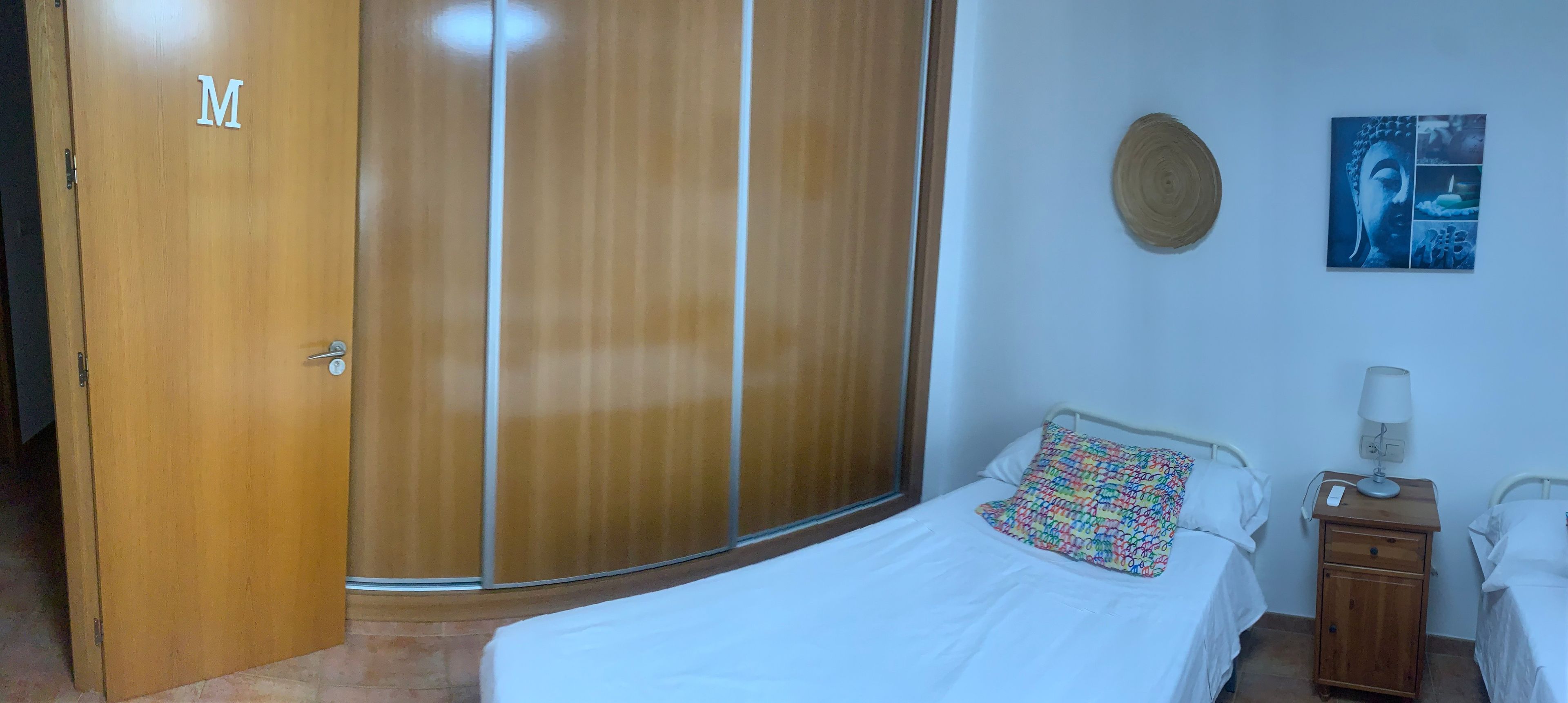 Un dormitorio con cama, mesita de noche, lámpara, armario y un cuadro colgado en la pared.
