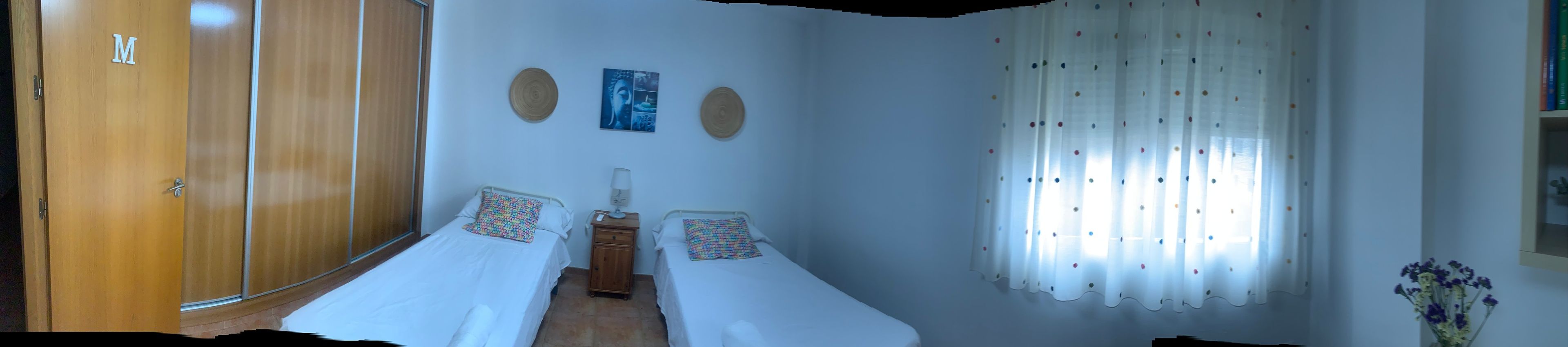 A room with two single beds, a wooden wardrobe, a small cabinet, and a window with curtains.