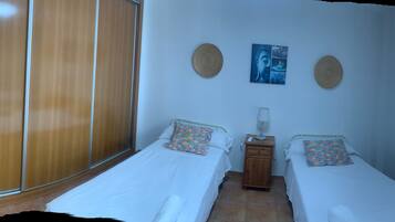 A room with two single beds, a wooden wardrobe, a small cabinet, and a window with curtains.