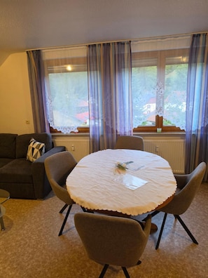 Una mesa redonda con mantel blanco, rodeada por cuatro sillas, en una habitación con vistas amplias desde grandes ventanales.