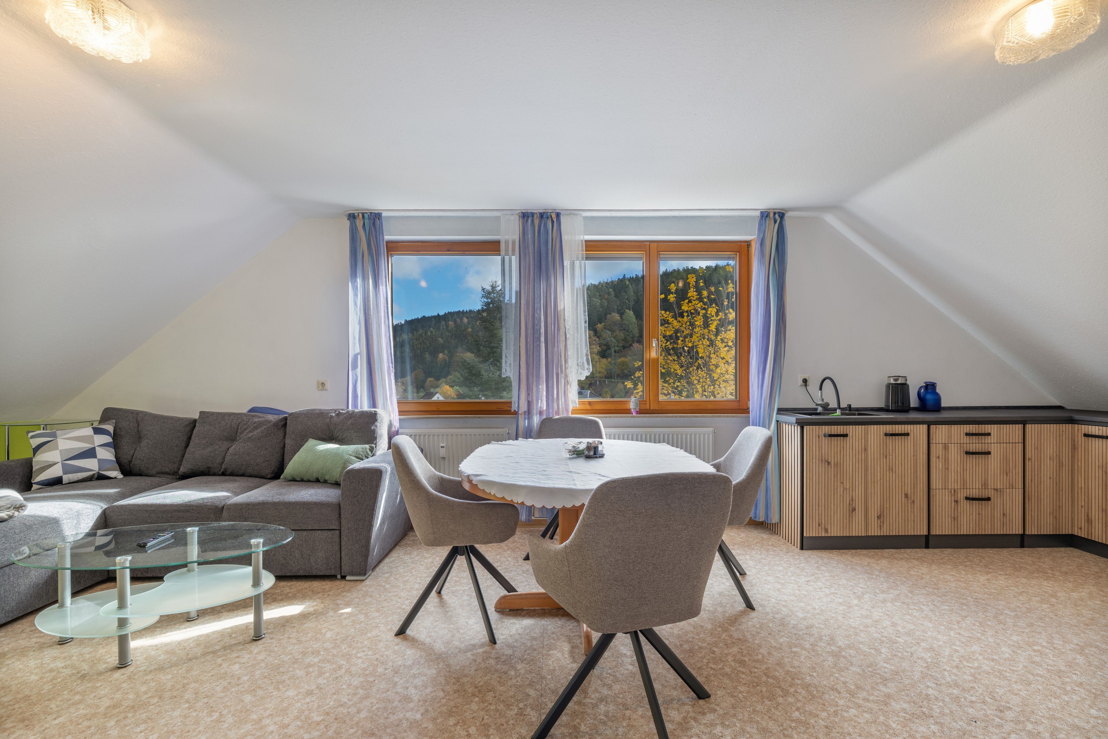 A modern loft bedroom with a sloped ceiling, a dining area with a round table, and a kitchenette.