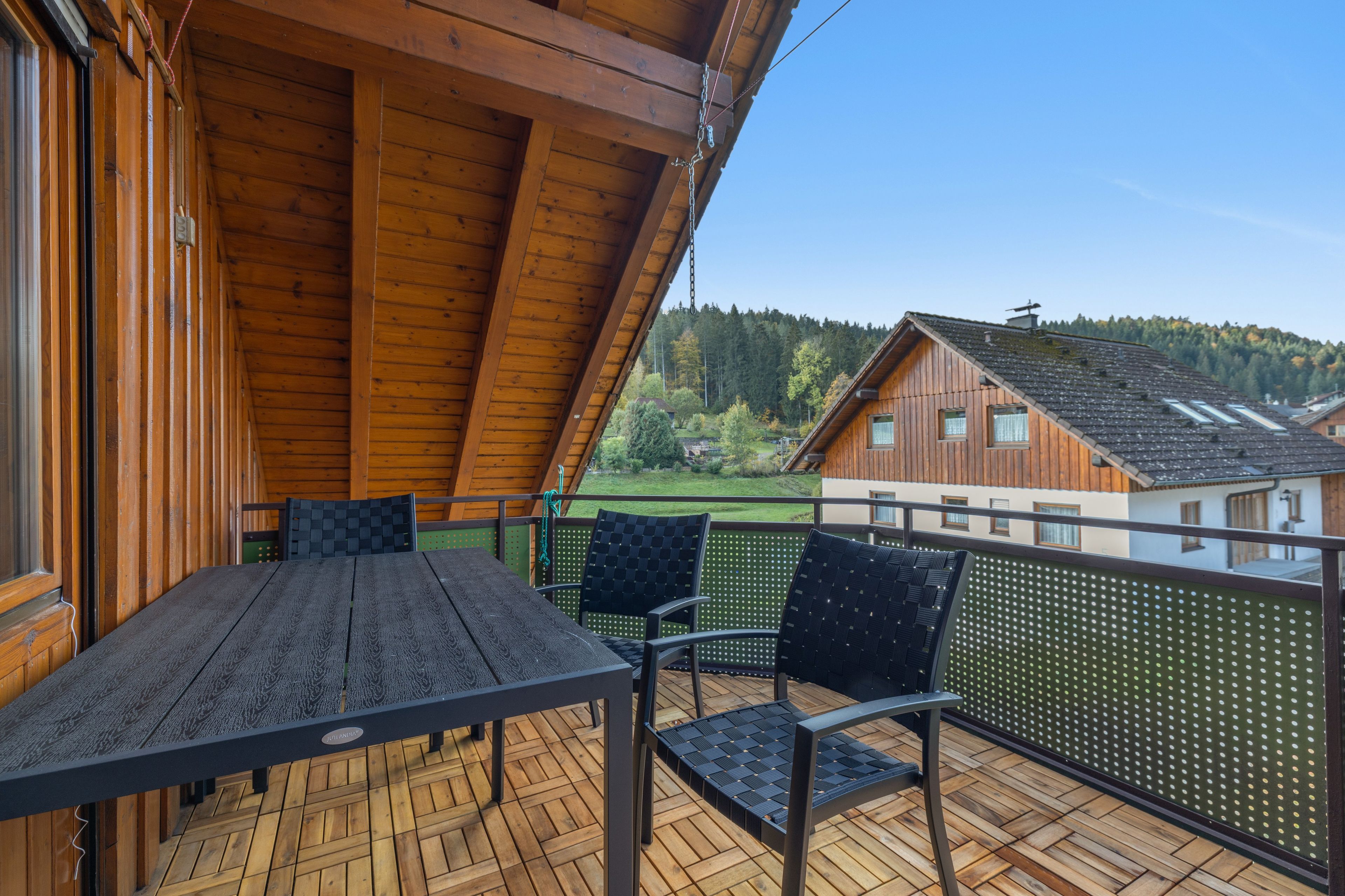 Eine Holzdielen-Terrasse mit Tisch und Stühlen mit Blick auf ein Wohngebiet und Hügel.