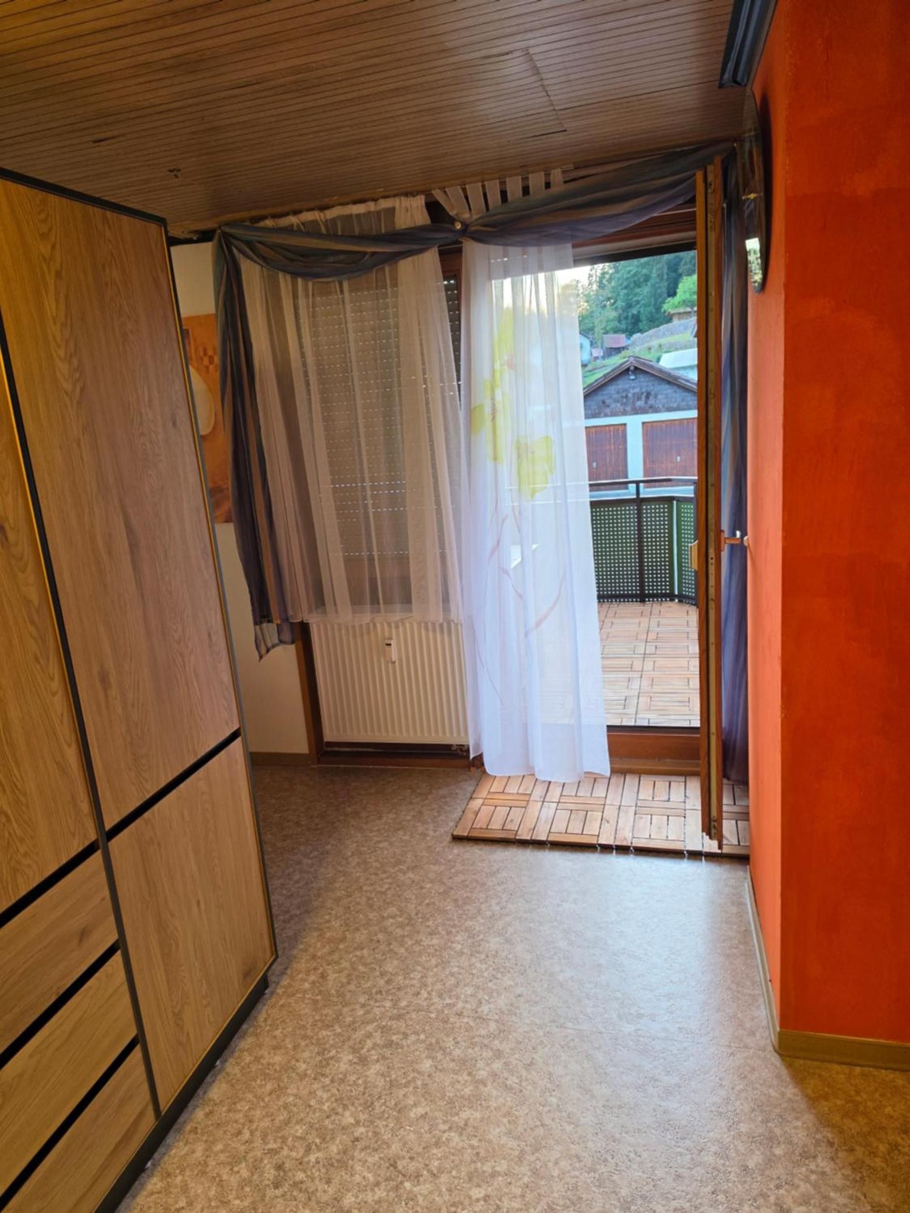 A room with a wooden wardrobe, a radiator, a tiled floor, and a door leading to an outdoor area.