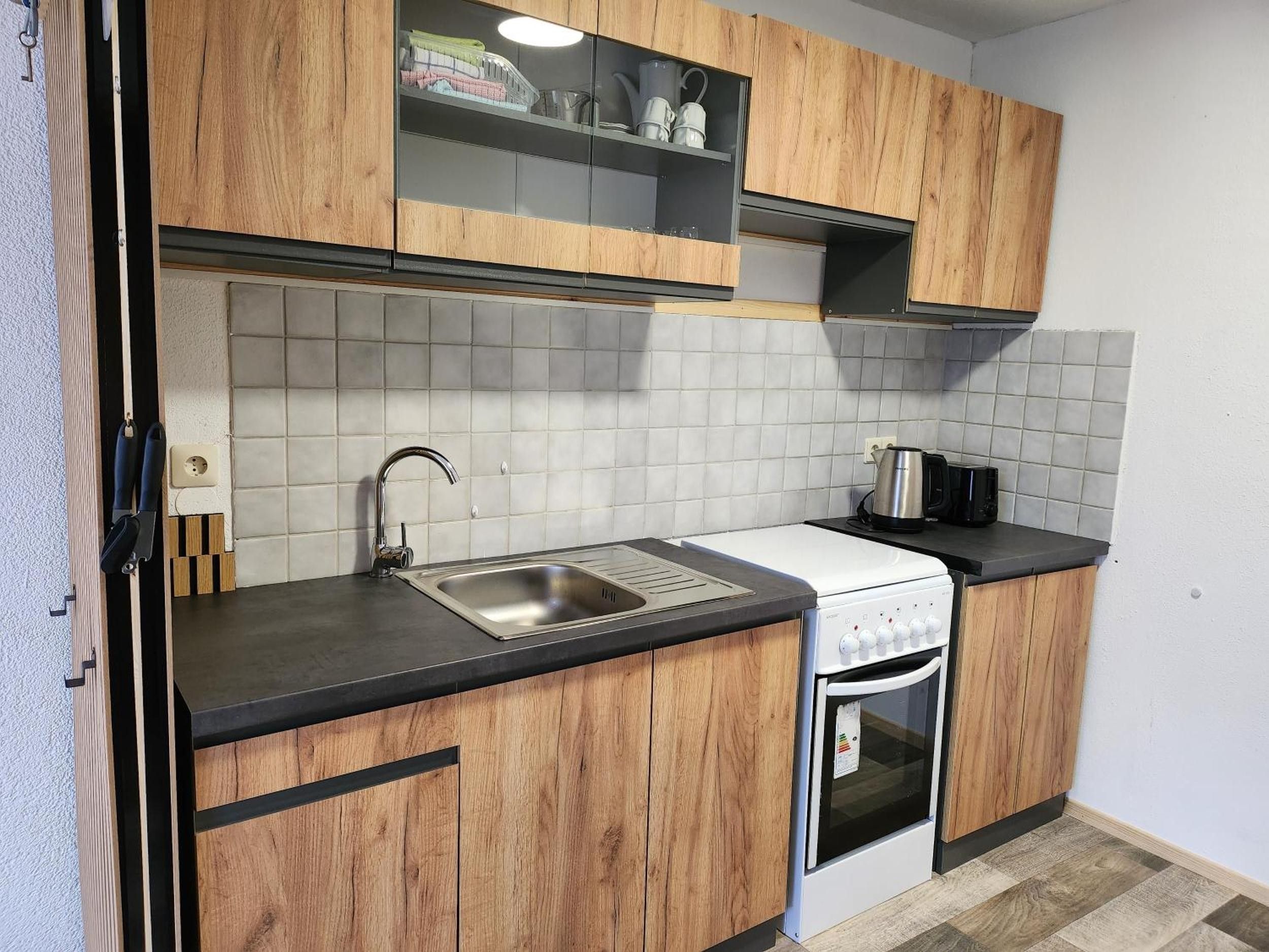 A kitchen with wooden cabinets, a stainless steel sink, a white stove, and a tiled backsplash.