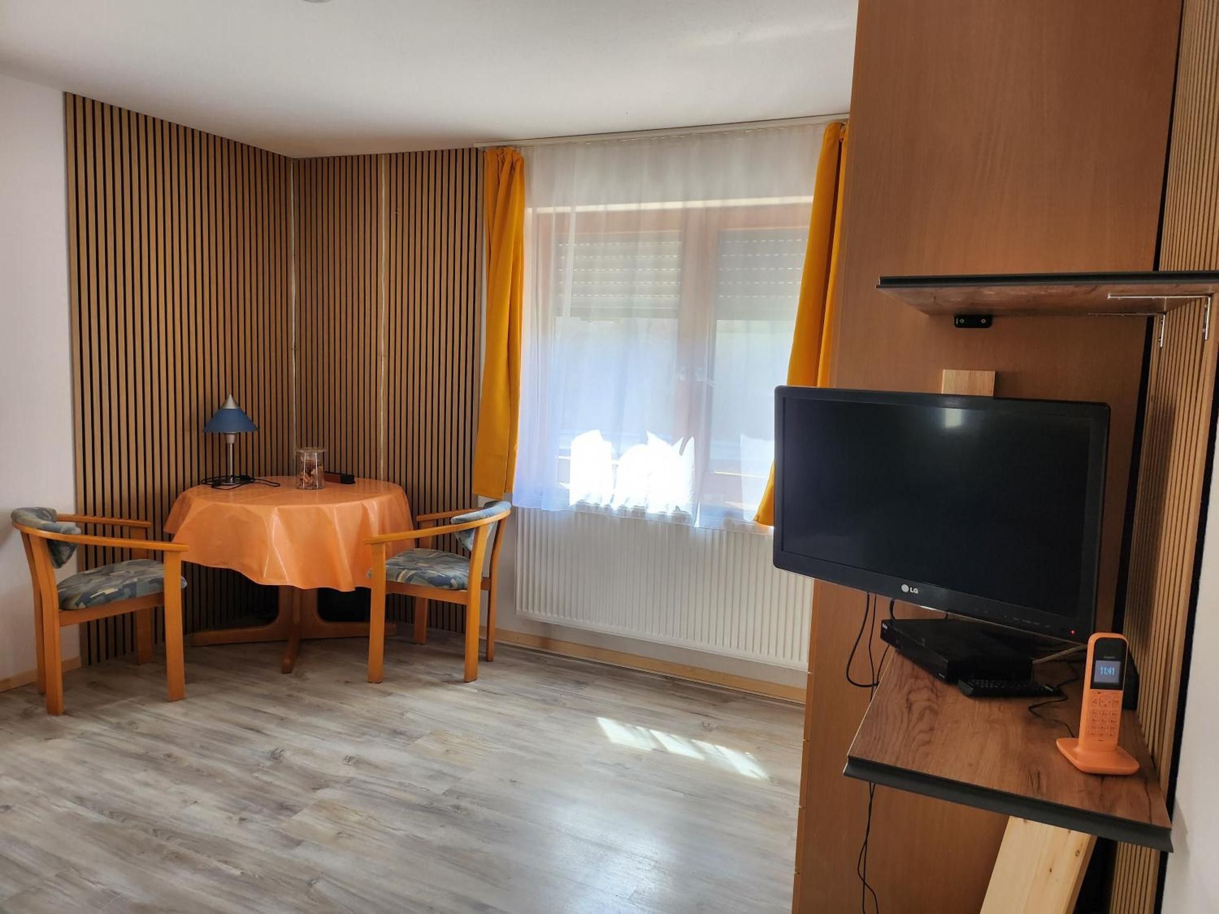 A room with a dining table, chairs, a television, and a telephone.