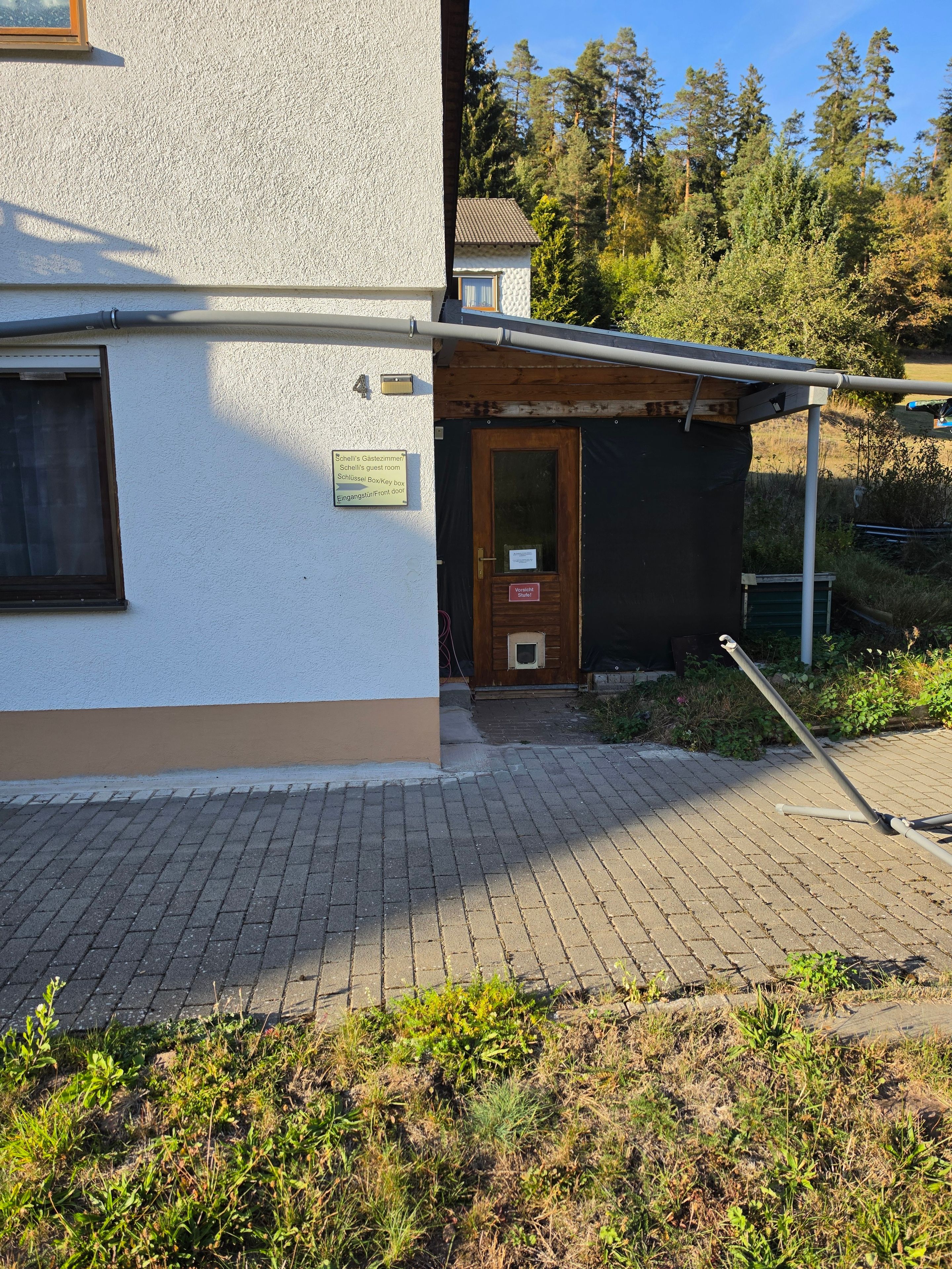 A building with a paved entrance, a wooden door, and a sign indicating guest rooms.