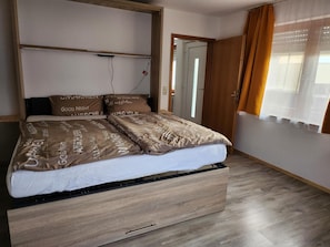 Een bed met houten frame en een opbergla, een nachtkastje en een raam met gordijnen.