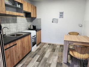Een kleine keuken met houten kastjes, een witte kookplaat en een betegelde achterwand.
