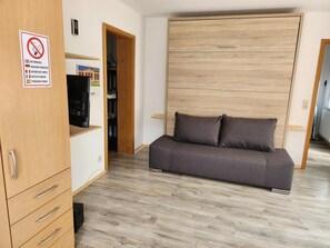 Een kamer met een bank, een kledingkast, een bordje ‘niet roken’ en een deur naar een inloopkast.
