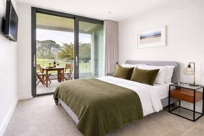 Una camera da letto con un letto, un comodino, una TV, una porta scorrevole in vetro che dà su un balcone e un quadro appeso al muro.