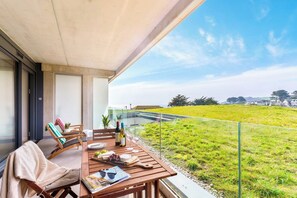 Ein Balkon mit Esstisch, der auf eine Wiese und Häuser blickt.