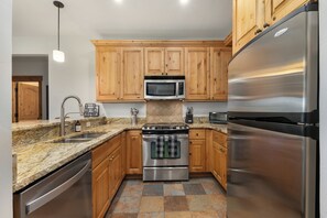 A modern kitchen with wooden cabinets, stainless steel appliances, a granite countertop, and a tiled backsplash. - Slopeside | Washer/Dryer | Hot Tub & Pool | On Bus Route (Steamboat Springs)