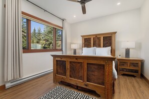 A bedroom with a wooden bed, two bedside tables, a window with curtains, and a ceiling fan. - Slopeside | Washer/Dryer | Hot Tub & Pool | On Bus Route (Steamboat Springs)