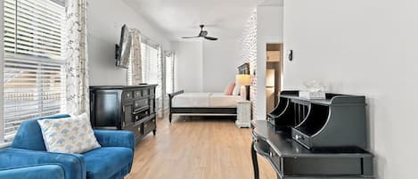 A room with a bed, a blue sofa, a black piano, and a ceiling fan.
