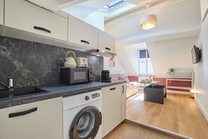 A modern kitchen with a built-in washing machine, a microwave, and a kettle. - Charming Studio - Center of Paris Montorgueil (Paris)