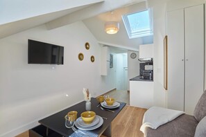 A modern kitchen with a built-in oven, a dining area with a table set for two, and a TV mounted on the wall. - Charming Studio - Center of Paris Montorgueil (Paris)