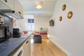 A modern kitchen with a built-in oven, microwave, and coffee machine. There is a dining area with a table and chairs, and a TV mounted on the wall. - Charming Studio - Center of Paris Montorgueil (Paris)